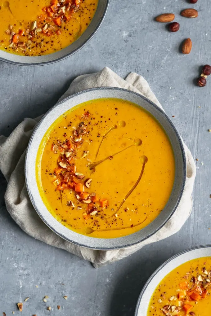 Butternut squash almond bisque with garnish of roasted squash, toasted, chopped almonds and hazelnuts, and a drizzle of olive oil