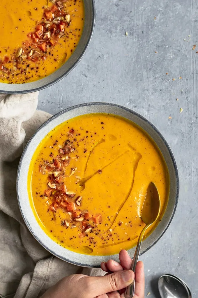 Butternut squash almond bisque with garnish of roasted squash, toasted, chopped almonds and hazelnuts, and a drizzle of olive oil