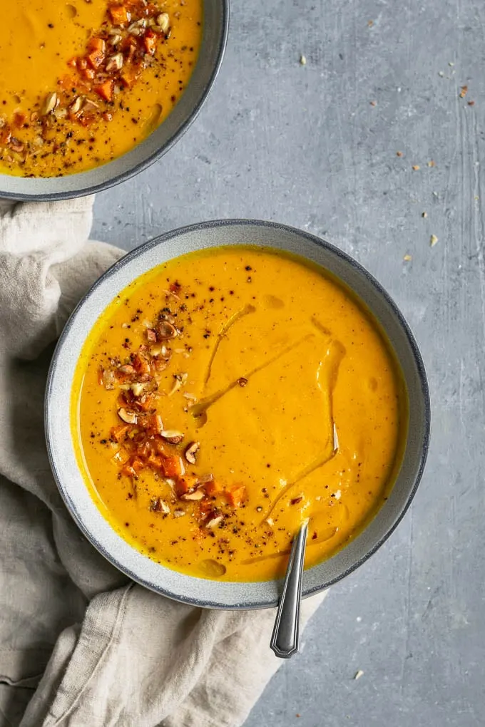 Butternut squash almond bisque with garnish of roasted squash, toasted, chopped almonds and hazelnuts, and a drizzle of olive oil