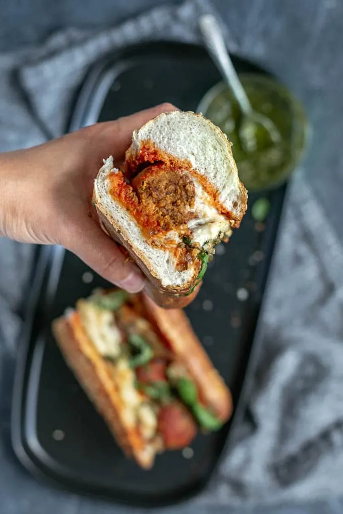 Vegan chickpea meatball subs with homemade mozzarella, pesto, and caramelized onions. View of the cut sandwich.