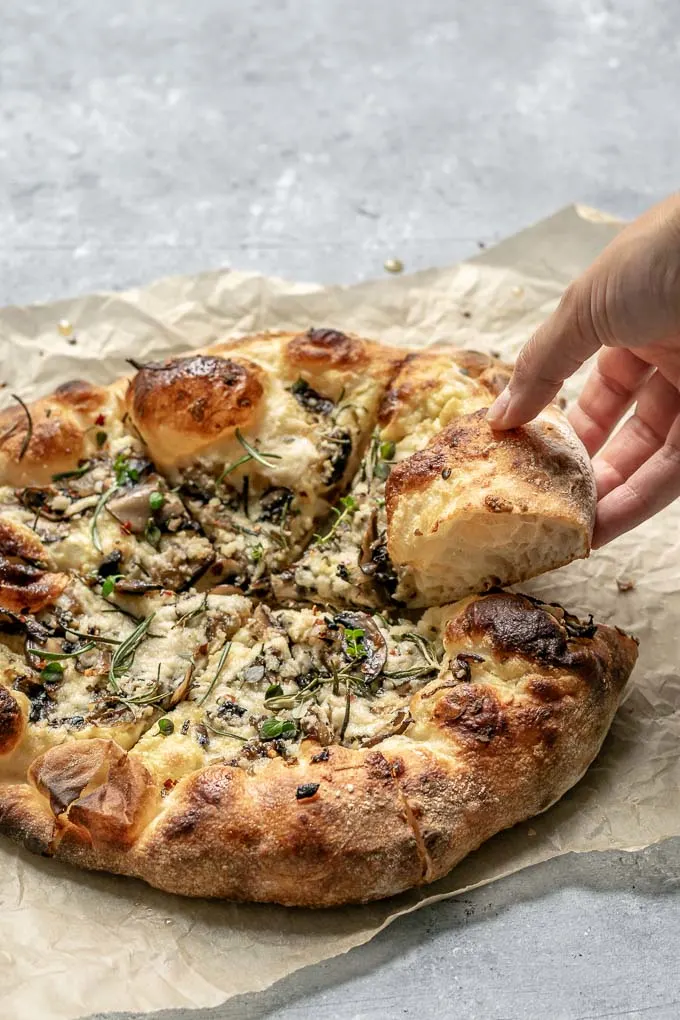 grabbing a slice of vegan caramelized mushroom and onion pizza with garlic white sauce and fresh rosemary