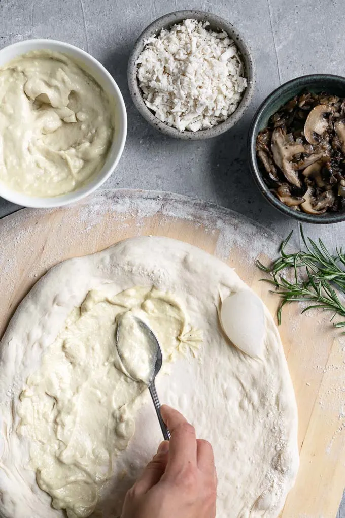 assembling the pizza, spreading garlic white sauce on the dough