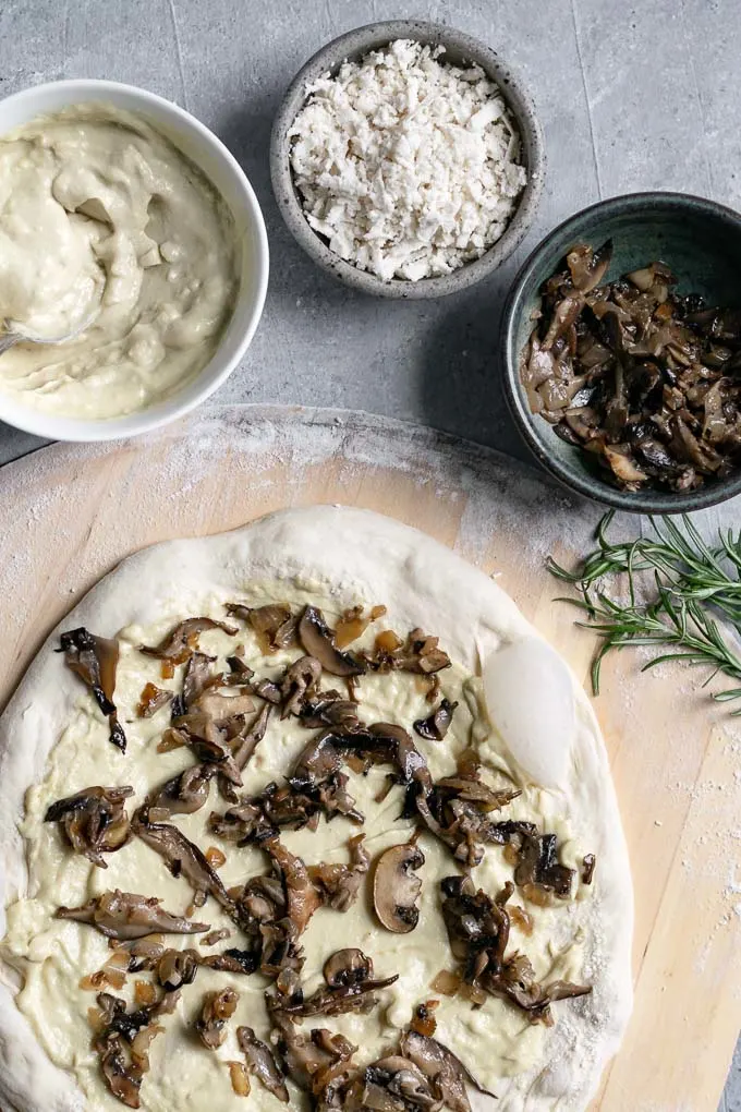 assembling the pizza with garlic white sauce and caramelized mushrooms on the dough