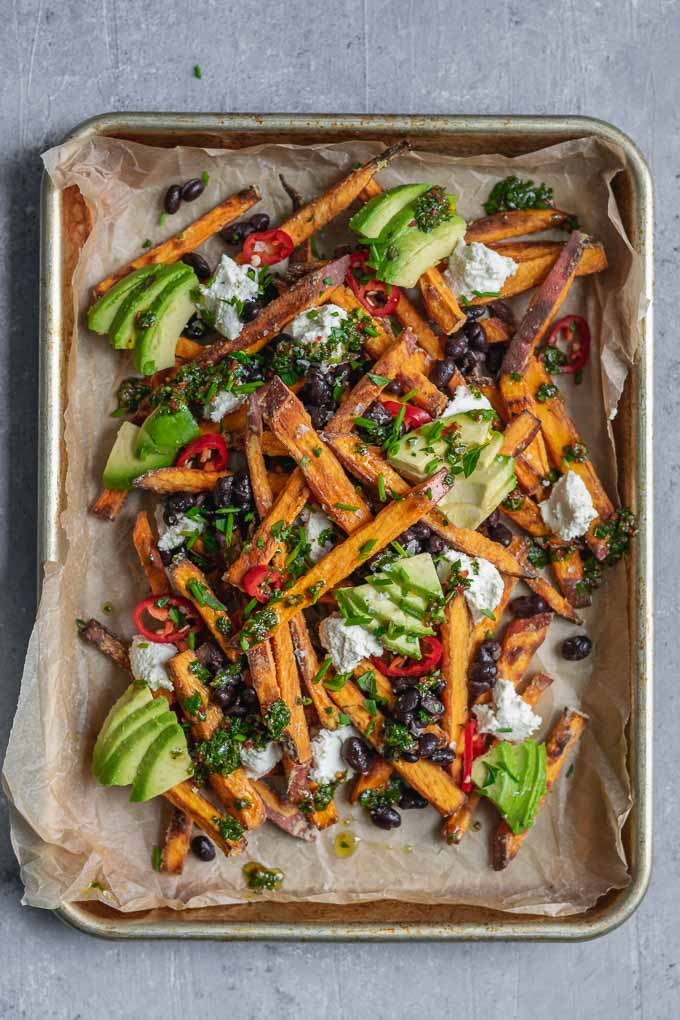 chimichurri loaded sweet potatoes with almond cheese, avocado, black beans, and sliced jalapeños