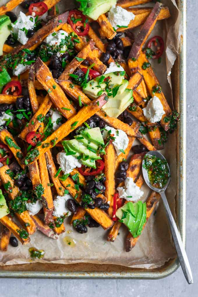 chimichurri loaded sweet potatoes with almond cheese, avocado, black beans, and sliced jalapeños