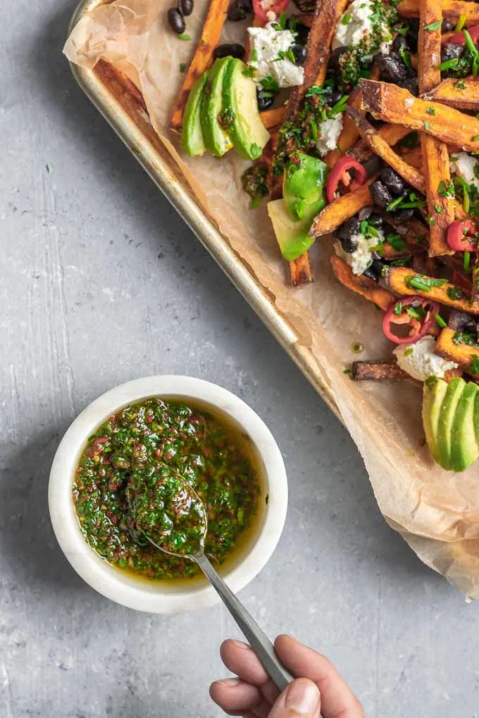 chimichurri loaded sweet potatoes with almond cheese, avocado, black beans, and sliced jalapeños