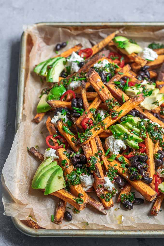 chimichurri loaded sweet potatoes with almond cheese, avocado, black beans, and sliced jalapeños