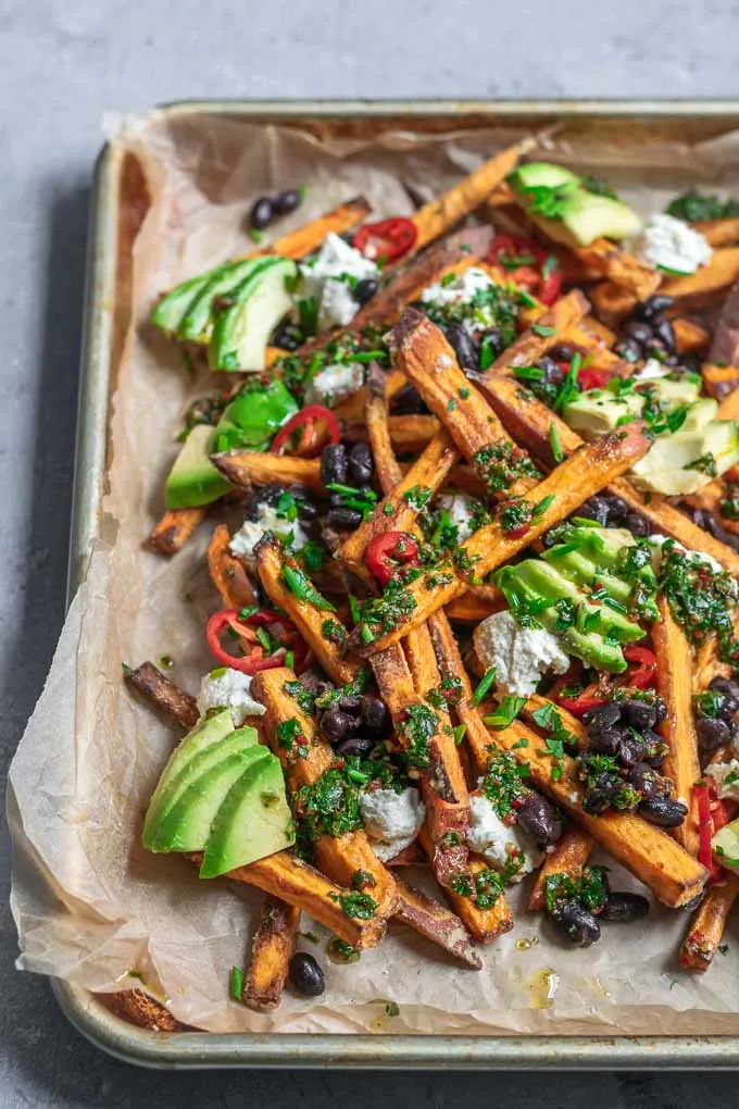 chimichurri loaded sweet potatoes with almond cheese, avocado, black beans, and sliced jalapeños