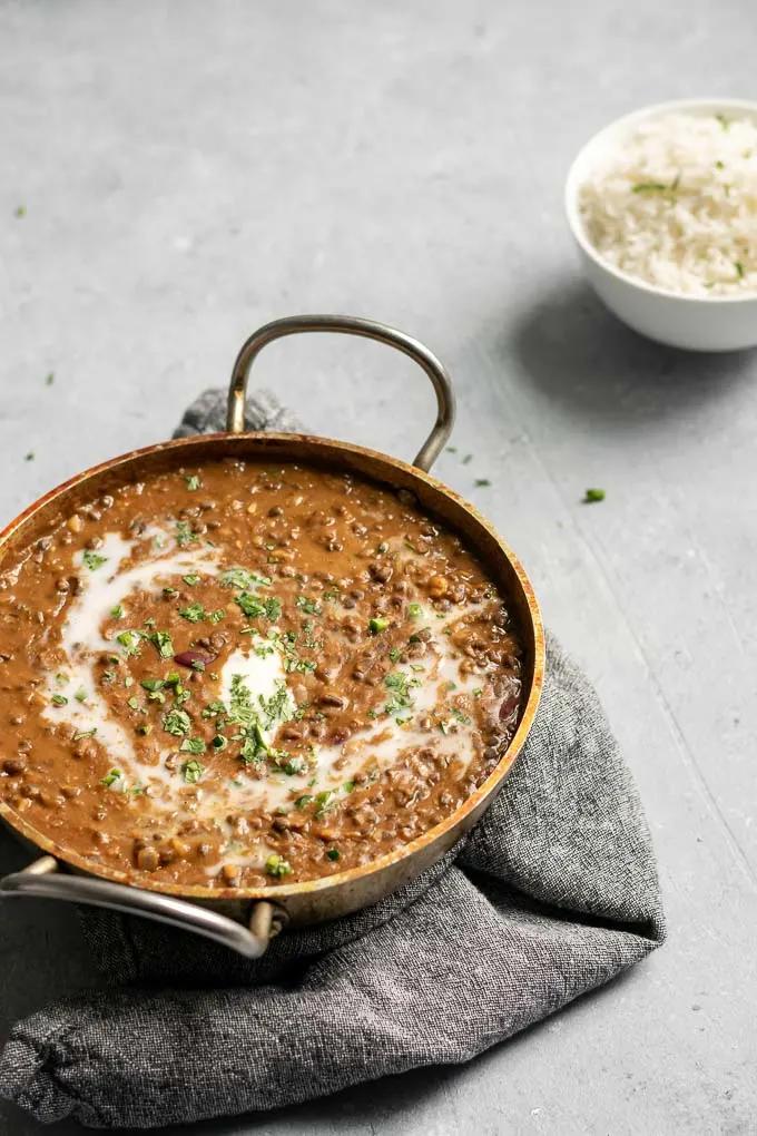 vegan dal makhani with a swirl of coconut milk and garnished with cilantro served with a bowl of basmati rice