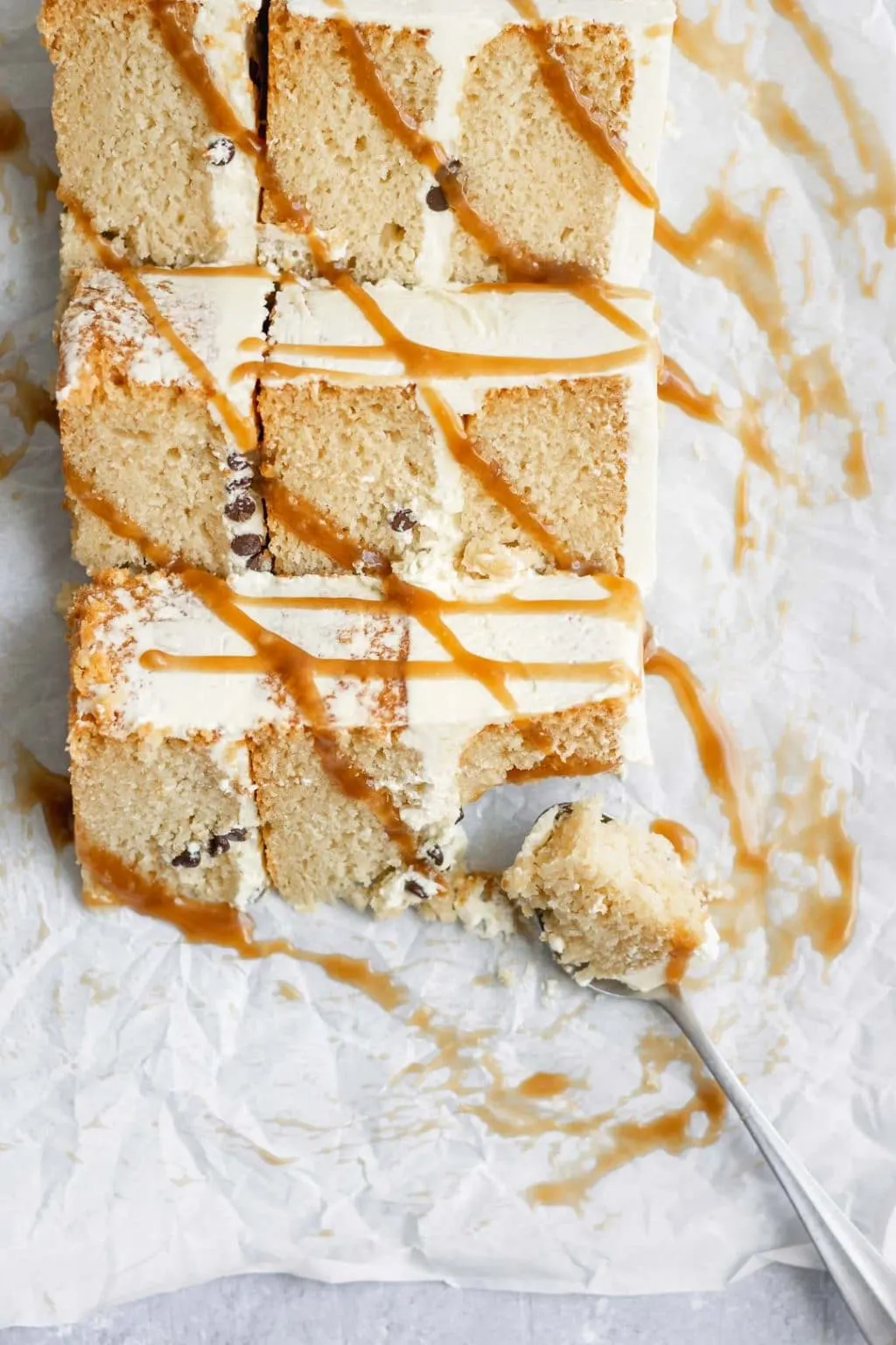 Three slices of vegan vanilla cake with a drizzle of salted caramel over the slices and a spoonful of one bite taken out of the cake