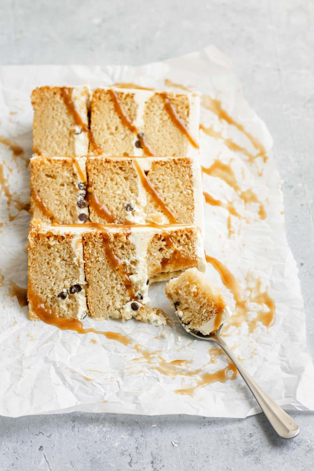 Three slices of vegan vanilla cake with a drizzle of salted caramel over the slices and a spoonful of one bite taken out of the cake