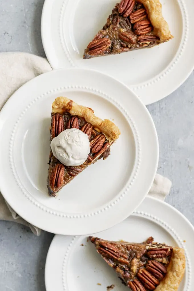 Three slices of vegan chocolate bourbon pecan pie with a scoop of vanilla ice cream