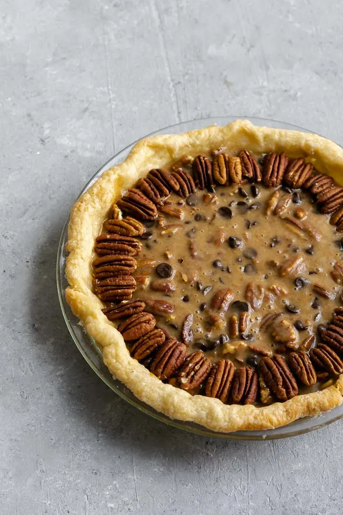 filled pie crust decorated with pecan halves before baking