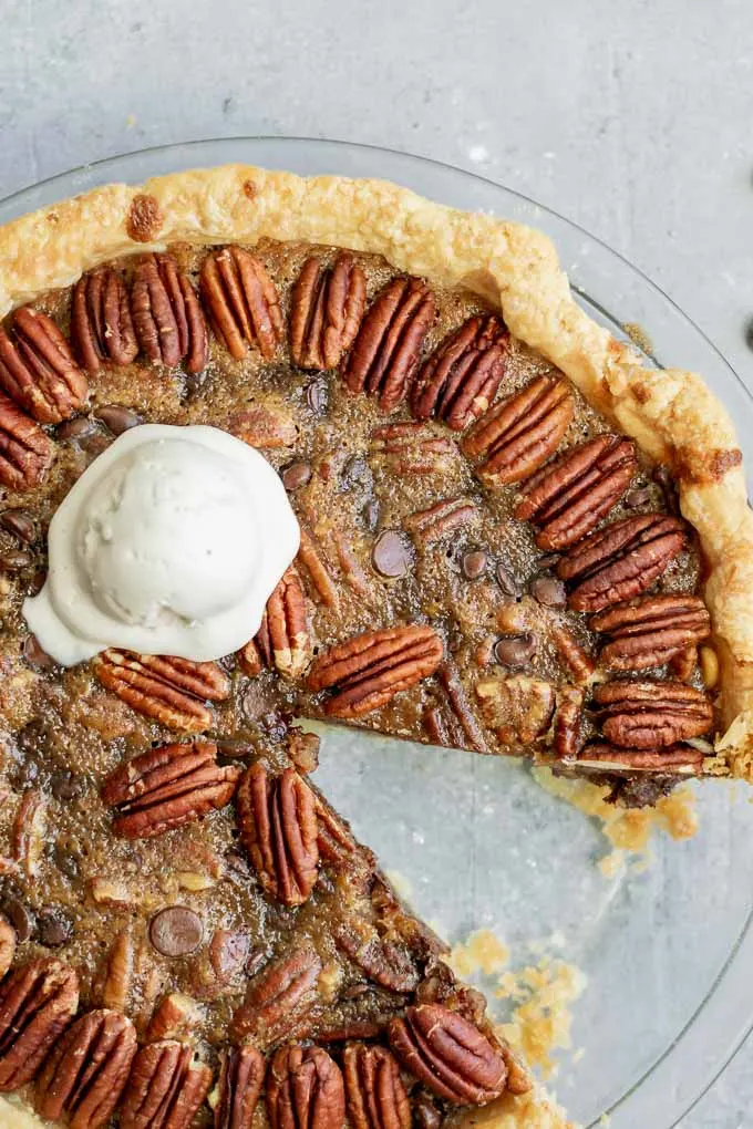 close up of a vegan chocolate bourbon pecan pie with a scoop of non-dairy vanilla ice cream and a slice taken out
