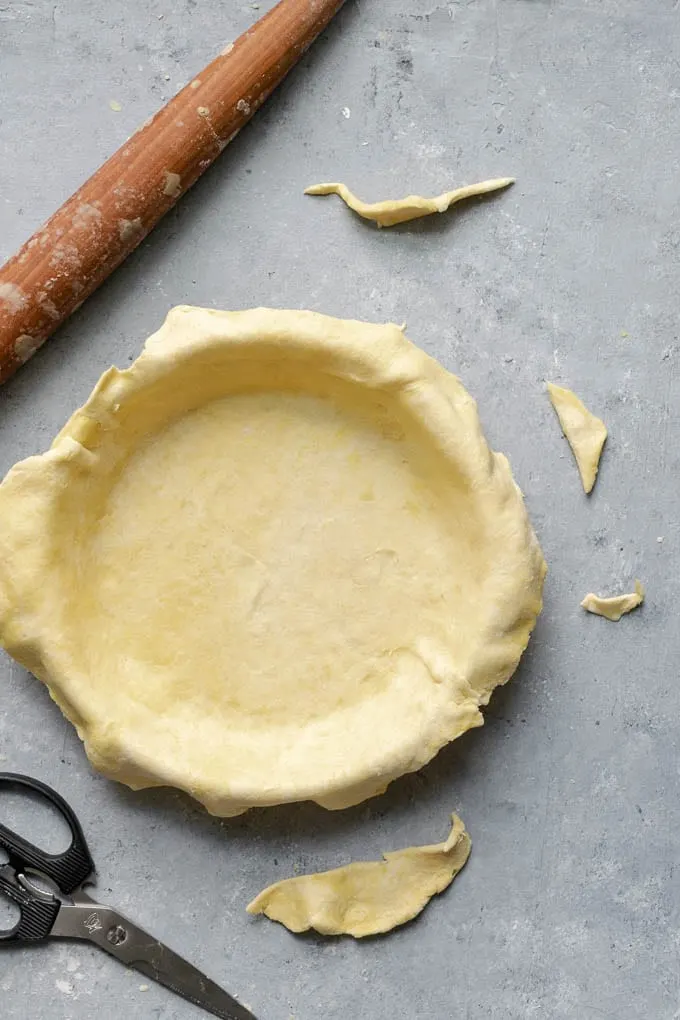 trimming off excess pie dough from edges of dish