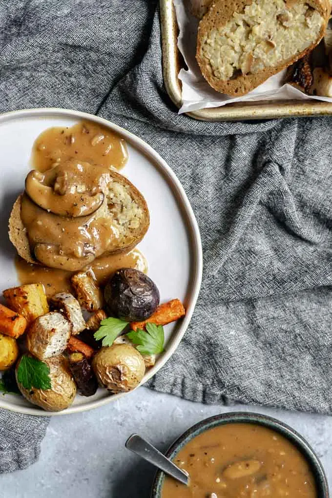 A slice of seitan roast stuffed with chestnut and white wine risotto topped with mushroom gravy and served with roasted vegetables