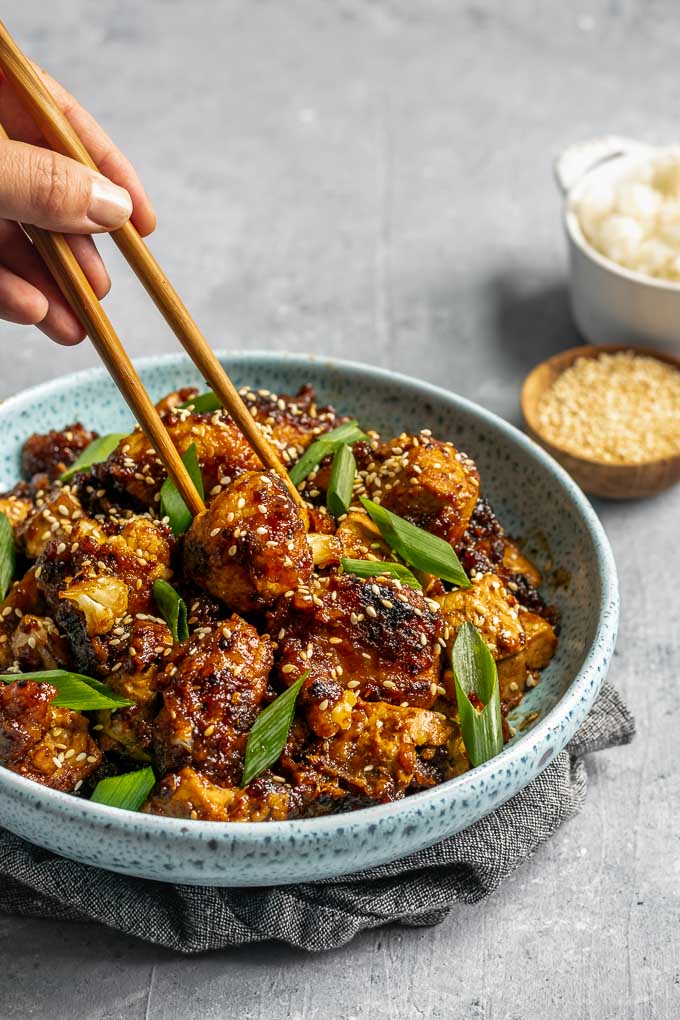 chopsticks grabbing a piece of sticky teriyaki tofu and cauliflower