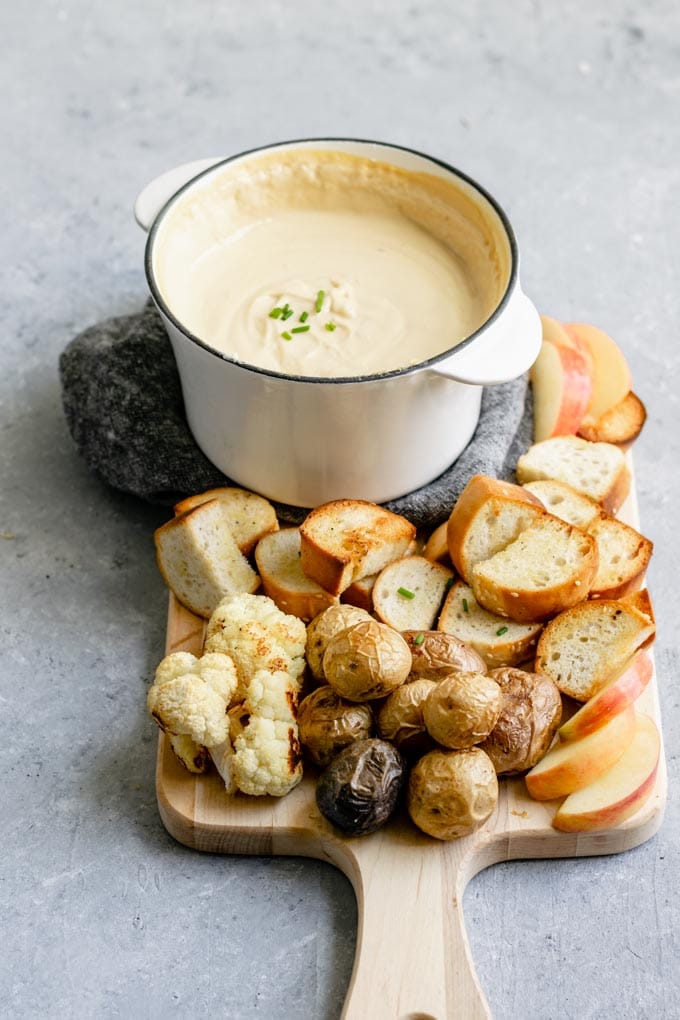 vegan cheese fondue served with toasted bread, roasted potatoes, roasted cauliflower, and slices of apple