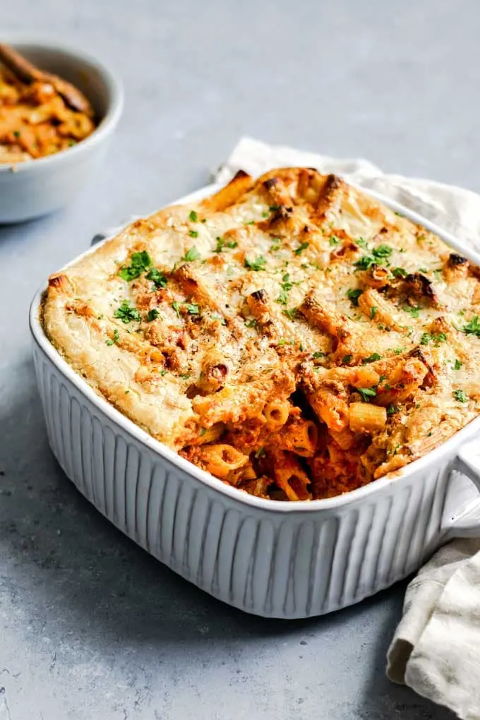 vegan baked ziti in a casserole dish with one serving in a bowl in the background