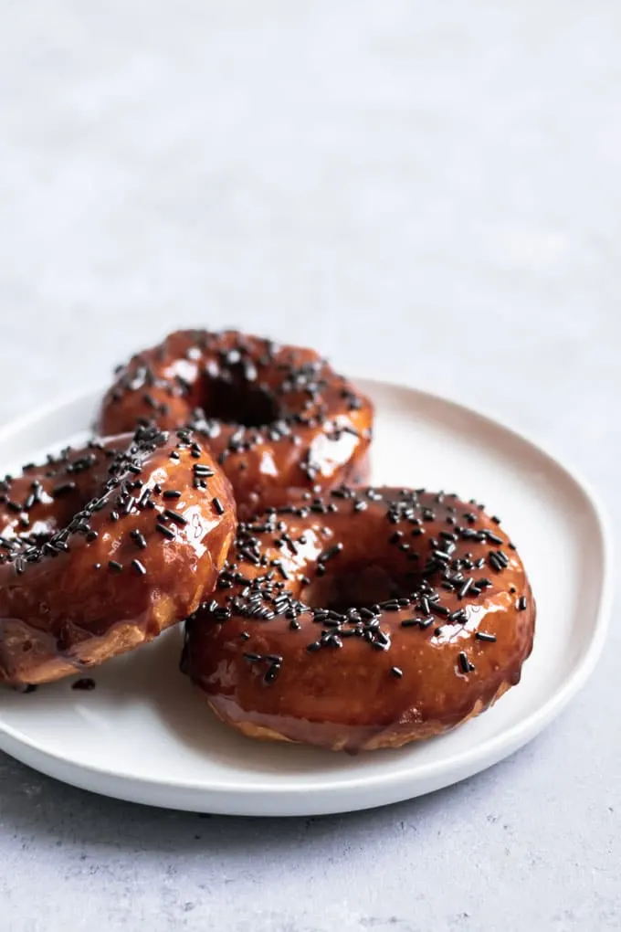 three vegan chocolate glazed doughnuts on a plate