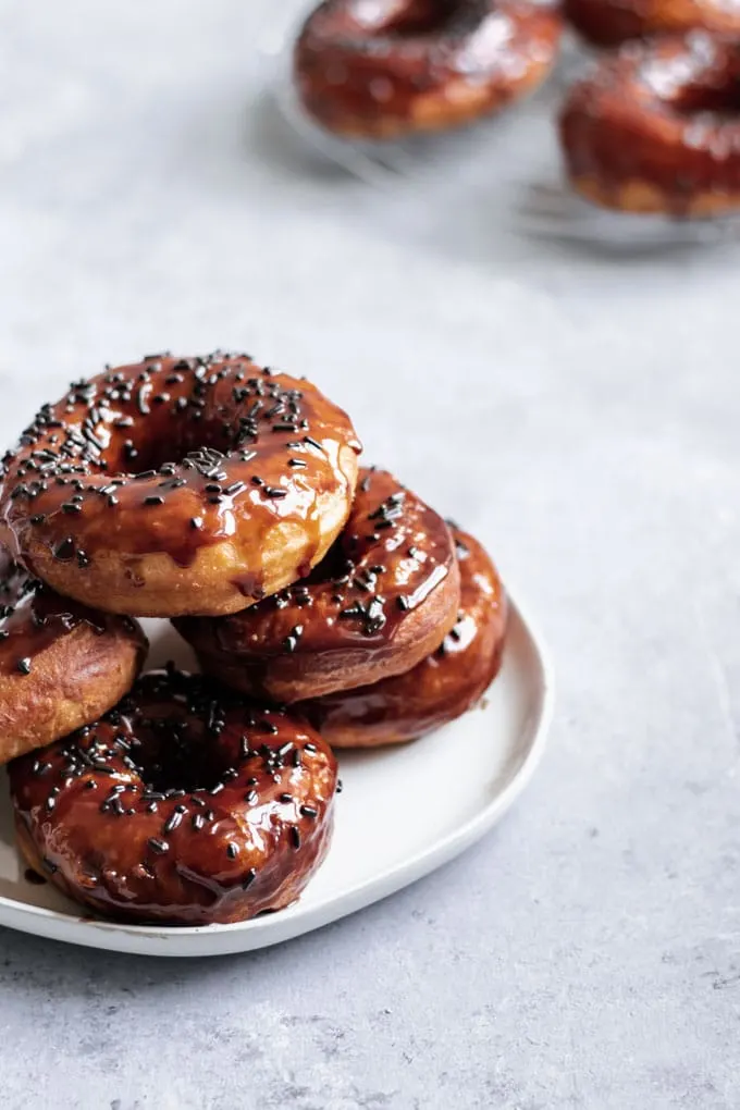 vegan chocolate glazed doughnuts stacked on a plate