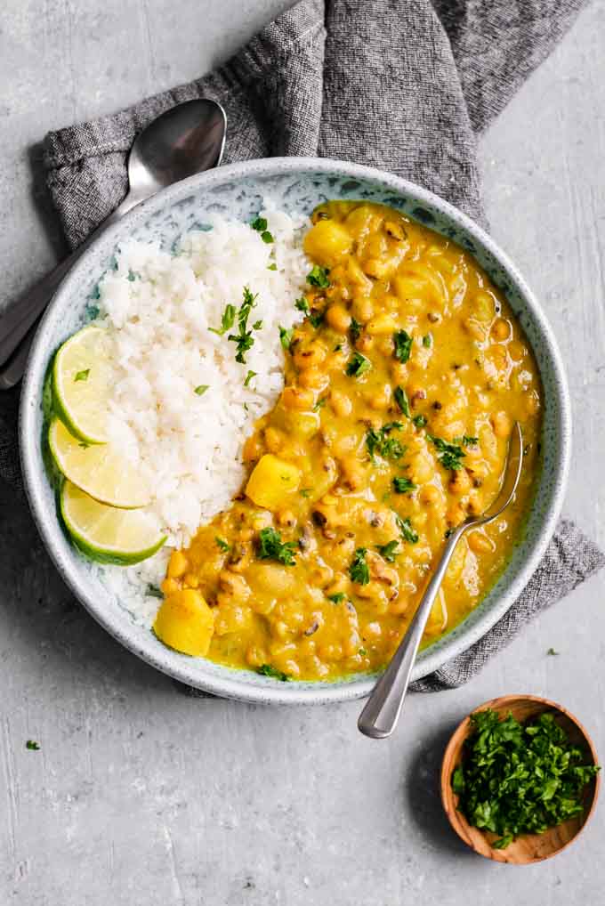 Jamaican black-eyed pea curry served with lime wedges and rice with a side of parsley for garnish