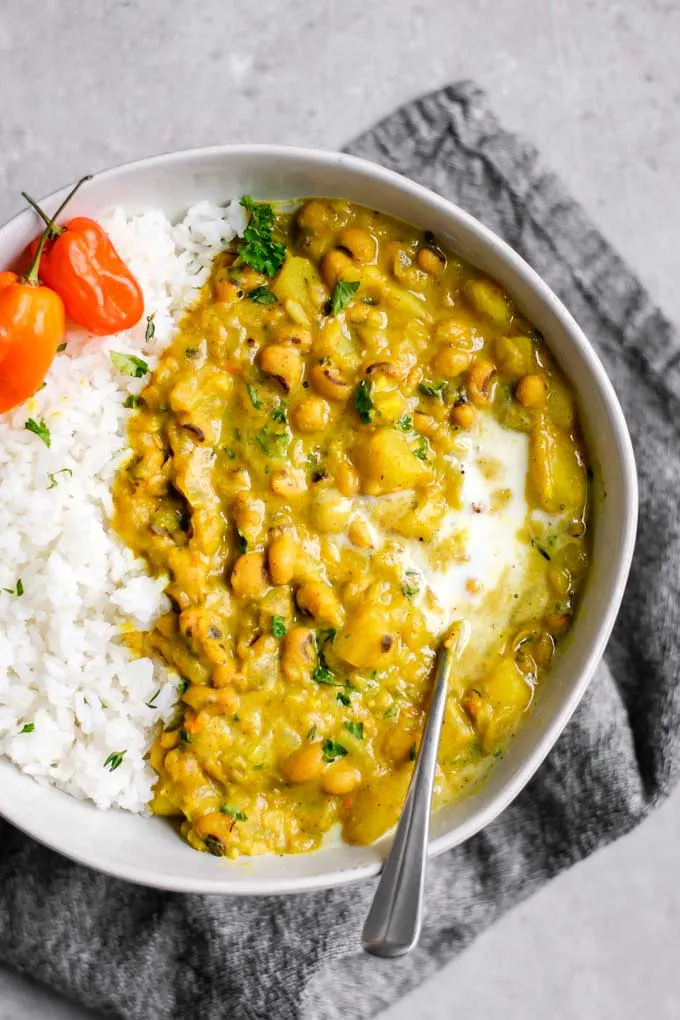 Jamaican black-eyed pea curry with rice and habanero peppers and a garnish of coconut milk and parsley overhead view