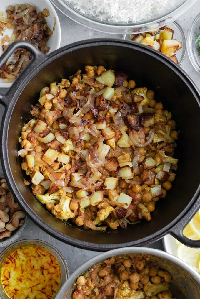 First layer of curry chickpeas and cauliflower, fried potatoes, and fried onions of Sindhi vegetable biryani