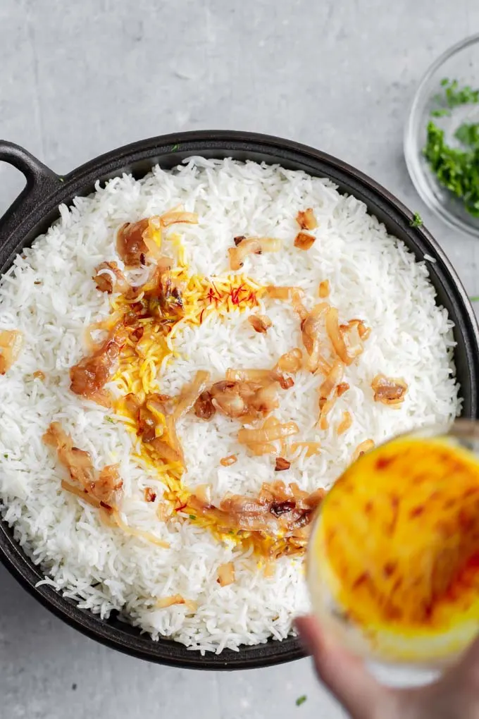 Drizzling the saffron infused plant milk over the final layer of rice and fried onions on Sindhi vegetable biryani