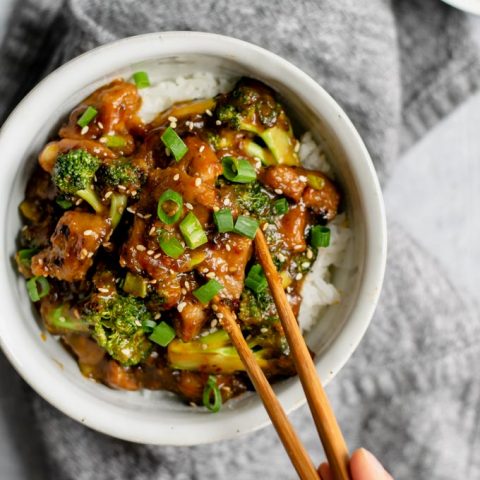 crispy orange seitan and broccoli with jasmine rice, grabbing a piece of seitan with chopsticks