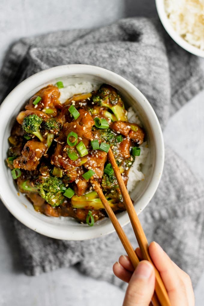 crispy orange seitan and broccoli with jasmine rice, grabbing a piece of seitan with chopsticks