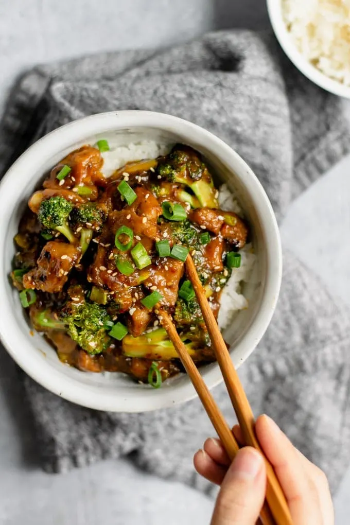 crispy orange seitan and broccoli with jasmine rice, grabbing a piece of seitan with chopsticks