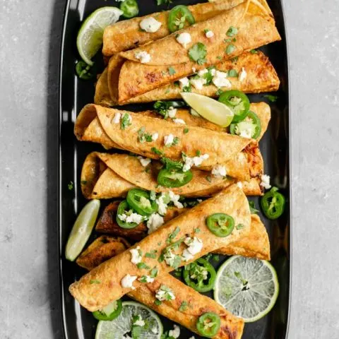 vegan cheesy beefy taquitos topped with cilantro, vegan queso fresco, jalapeños, and served with wedges of lime