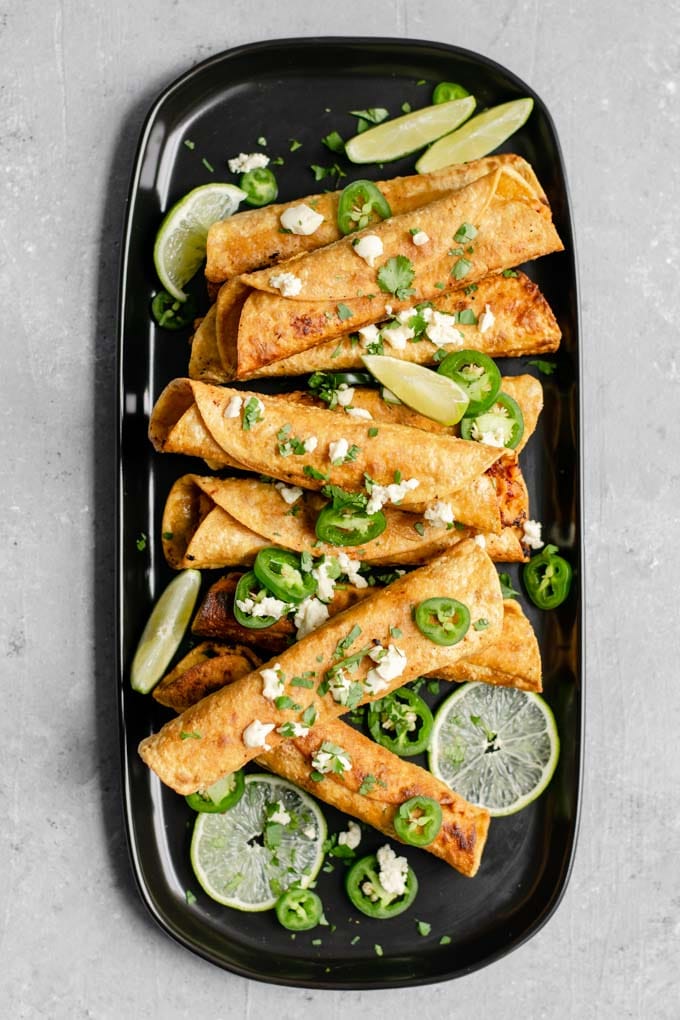 vegan cheesy beefy taquitos topped with cilantro, vegan queso fresco, jalapeños, and served with wedges of lime