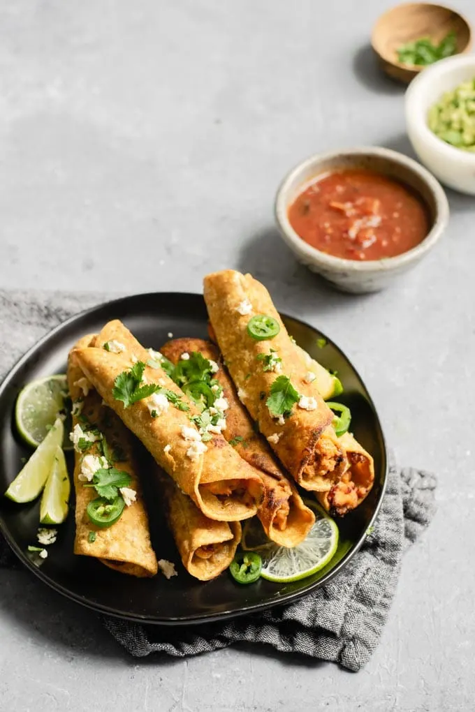 vegan cheesy beefy taquitos on a plate with bowls of salsa and guacamole for dipping