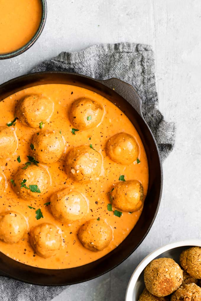 vegan chickpea meatballs in a roasted red pepper sauce cooked in a cast iron skillet with extra sauce and meatballs on the side