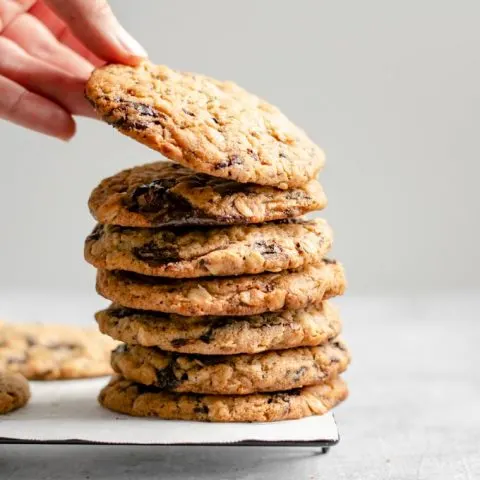 grabbing a cookie off the top of a stack of vegan peanut butter oatmeal chocolate chip cookies