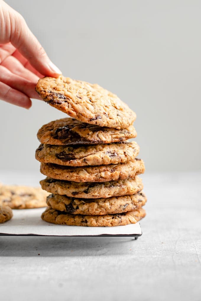 grabbing a cookie off the top of a stack of vegan peanut butter oatmeal chocolate chip cookies