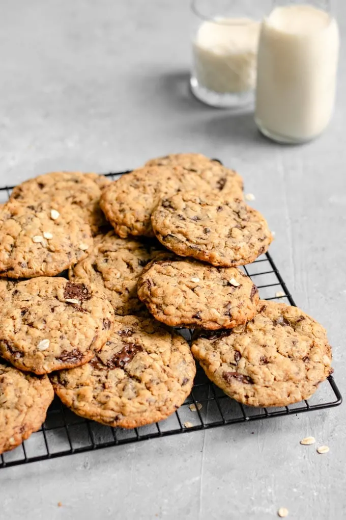 vegan peanut butter oatmeal chocolate chip cookies on a cooling rack with two glasses of soy milk