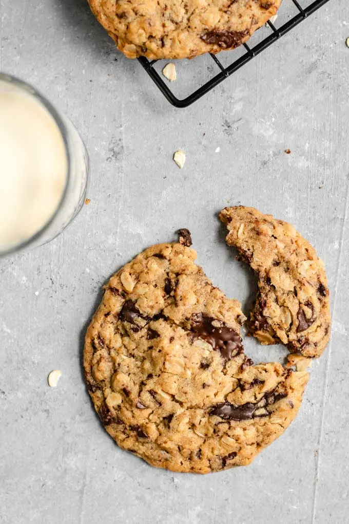 vegan peanut butter oatmeal chocolate chip cookie broken in half with a glass of soymilk