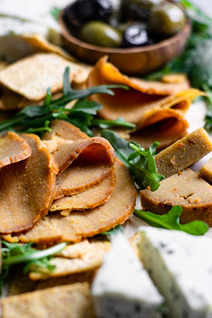 close up of the peppercorn and sun dried tomato homemade seitan deli meat cut into slices and wedges on a vegan cheese board