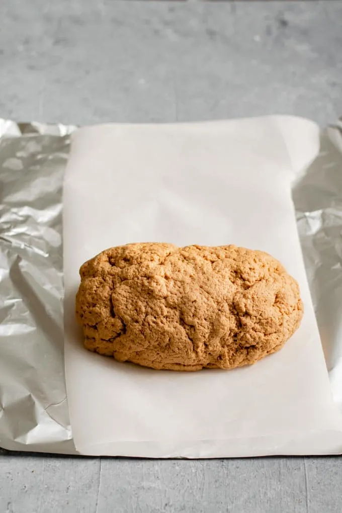 seitan dough sitting on prepared parchment paper lined aluminum foil. The seitan dough has been kneaded and shaped into a log. 