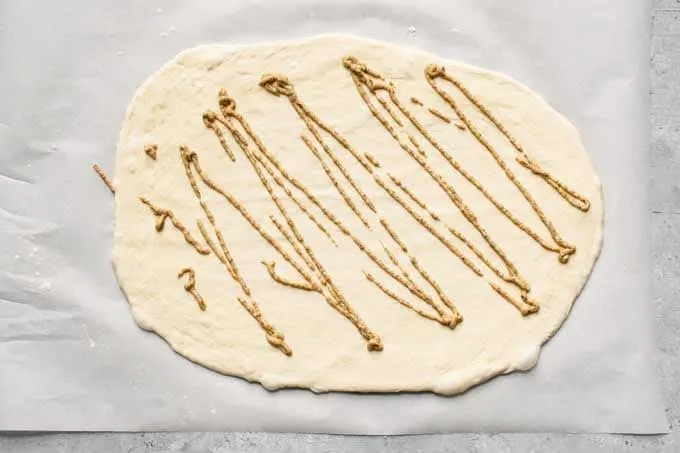 pizza dough rolled out and topped with grainy mustard for stromboli