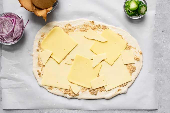 pizza dough topped with mustard and vegan cheese slices