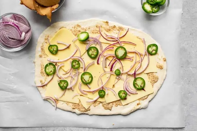 pizza dough topped with mustard, vegan cheese slices, jalapeño and red onion for stromboli