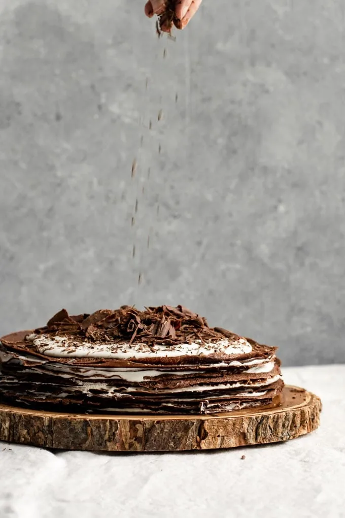 sprinkling chocolate shavings over a boozy vegan chocolate crepe cake