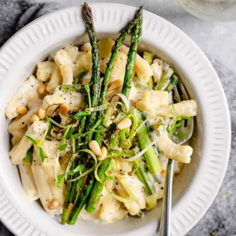 a bowlful of creamy asparagus and leek pasta served with a glass of wine