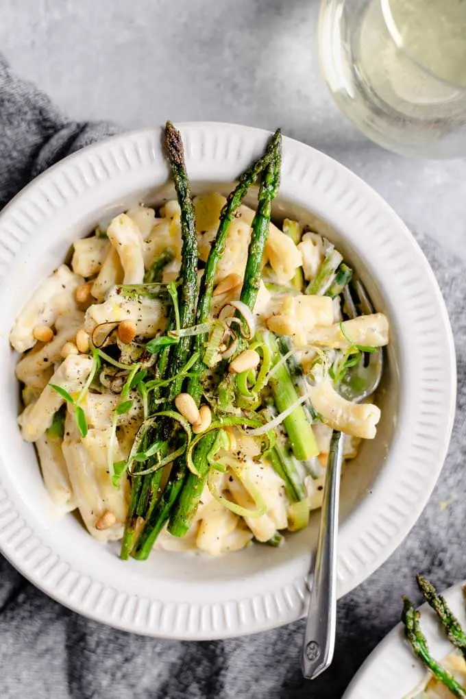 a bowlful of creamy asparagus and leek pasta served with a glass of wine
