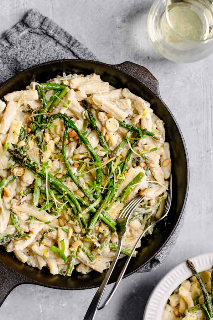 creamy asparagus and leek pasta served from a cast iron skillet and topped with asparagus spears, microgreens, and some fried leeks