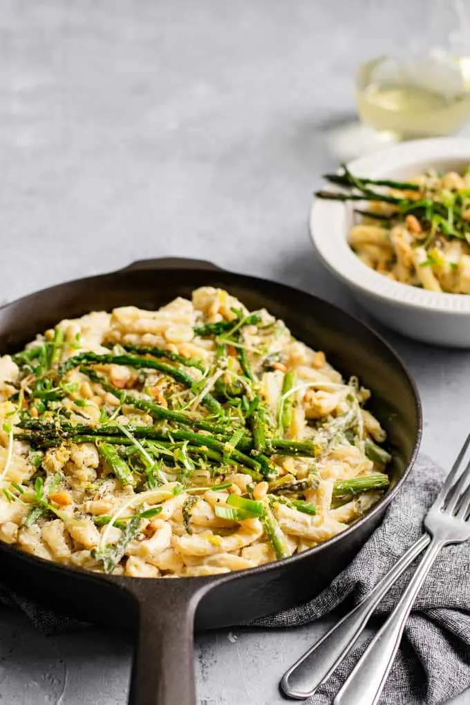 asparagus and leek pasta in a cast iron skillet with a bowl served along with a glass of wine